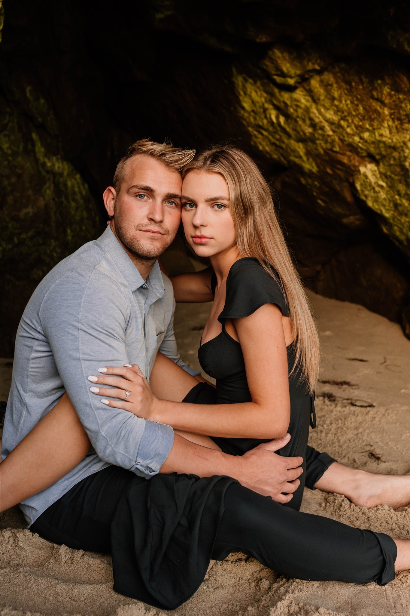 couple posing and looking at a camera on a cave on a beach