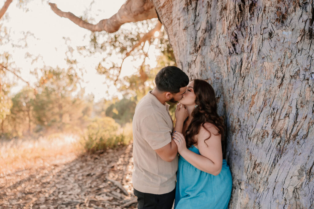 Couple kissing while leaning against a tree