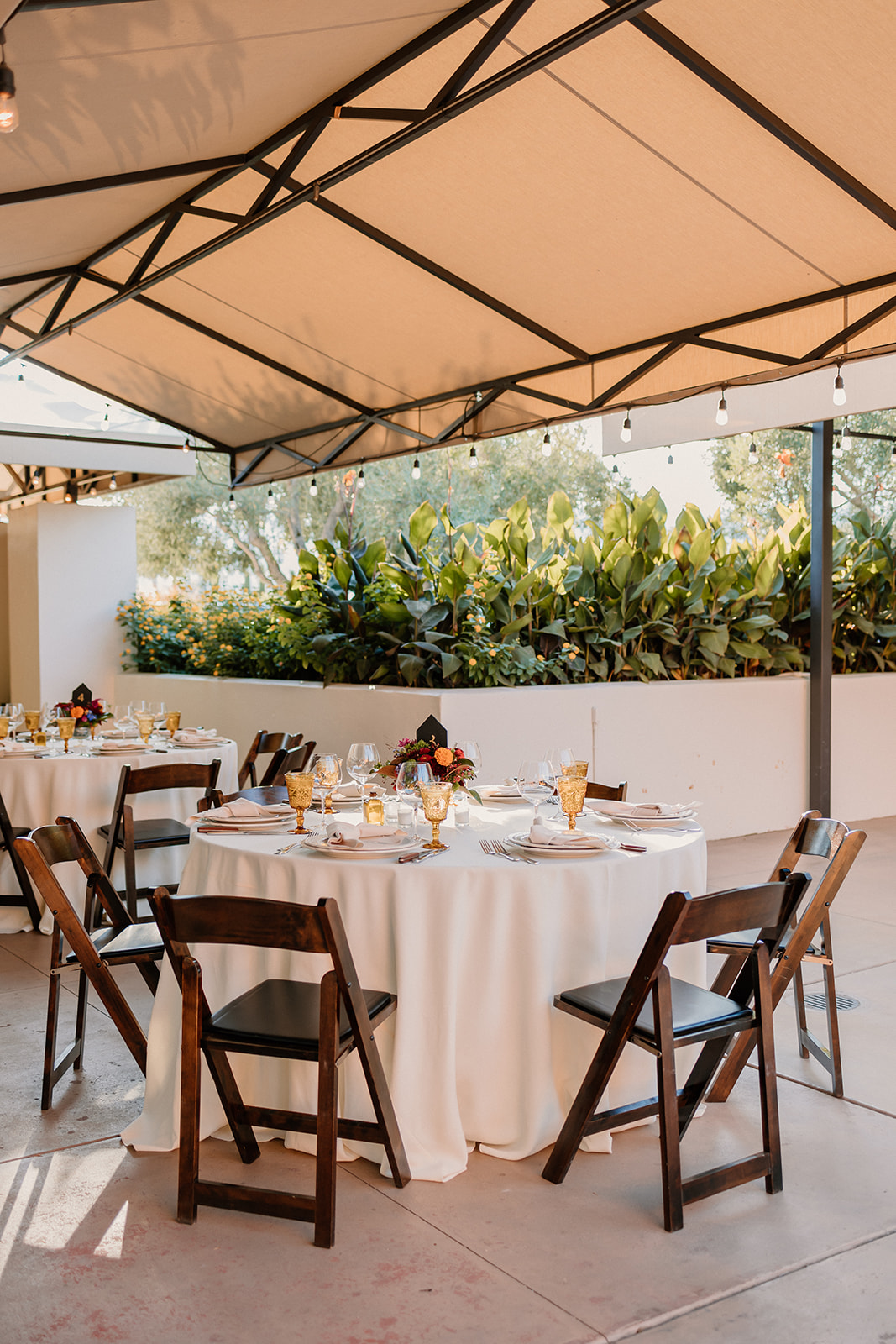 Outdoor dining setup under a canopy with elegantly set tables, wooden chairs, and lush greenery in the background at Tre Posti