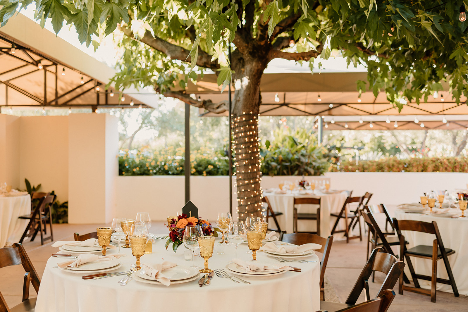 Outdoor dining setup under a canopy with elegantly set tables, wooden chairs, and lush greenery in the background at Tre Posti
