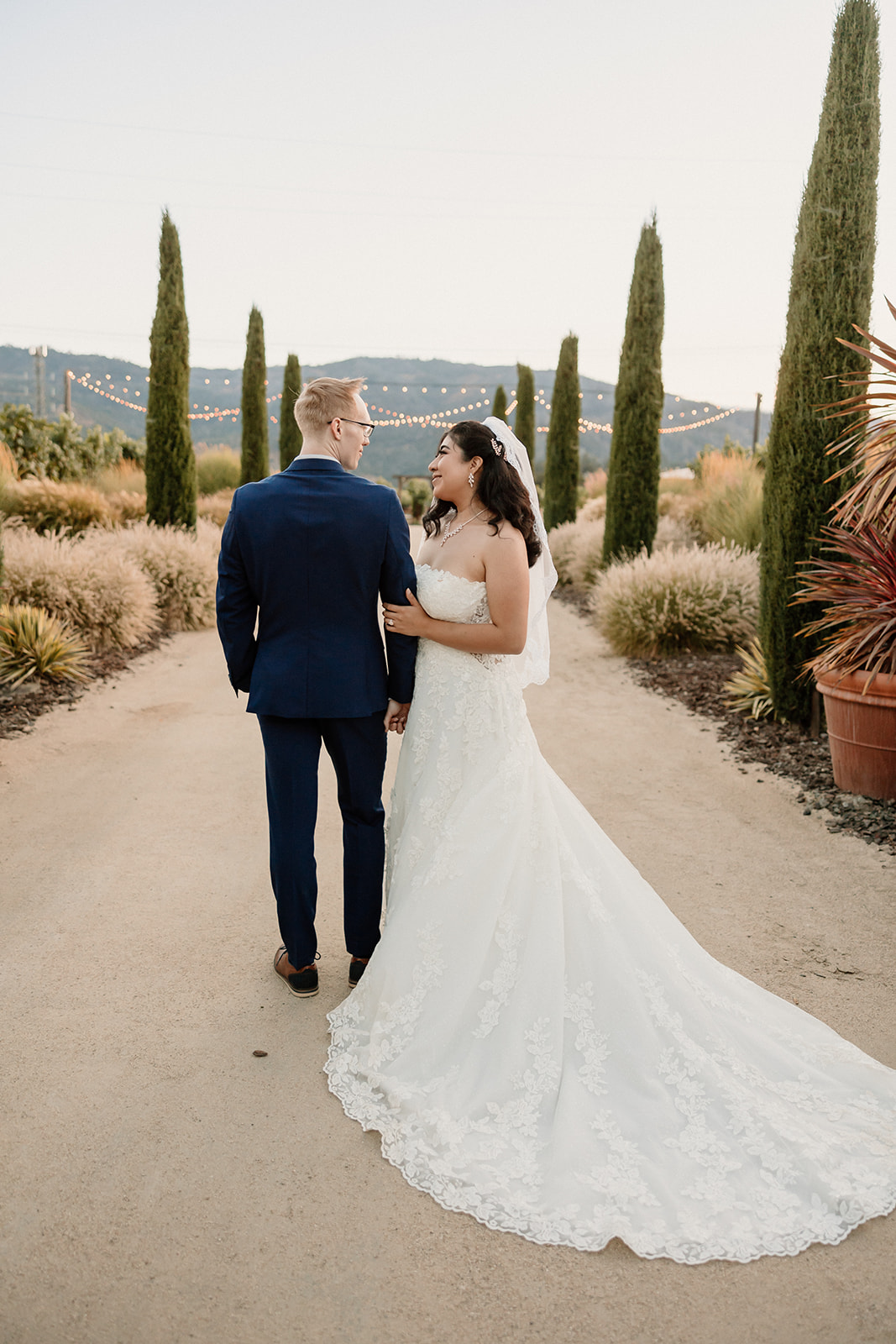 A bride and groom walking hand in hand outdoors, surrounded by cacti, with the bride looking at the groom at their Tre Posti Wedding