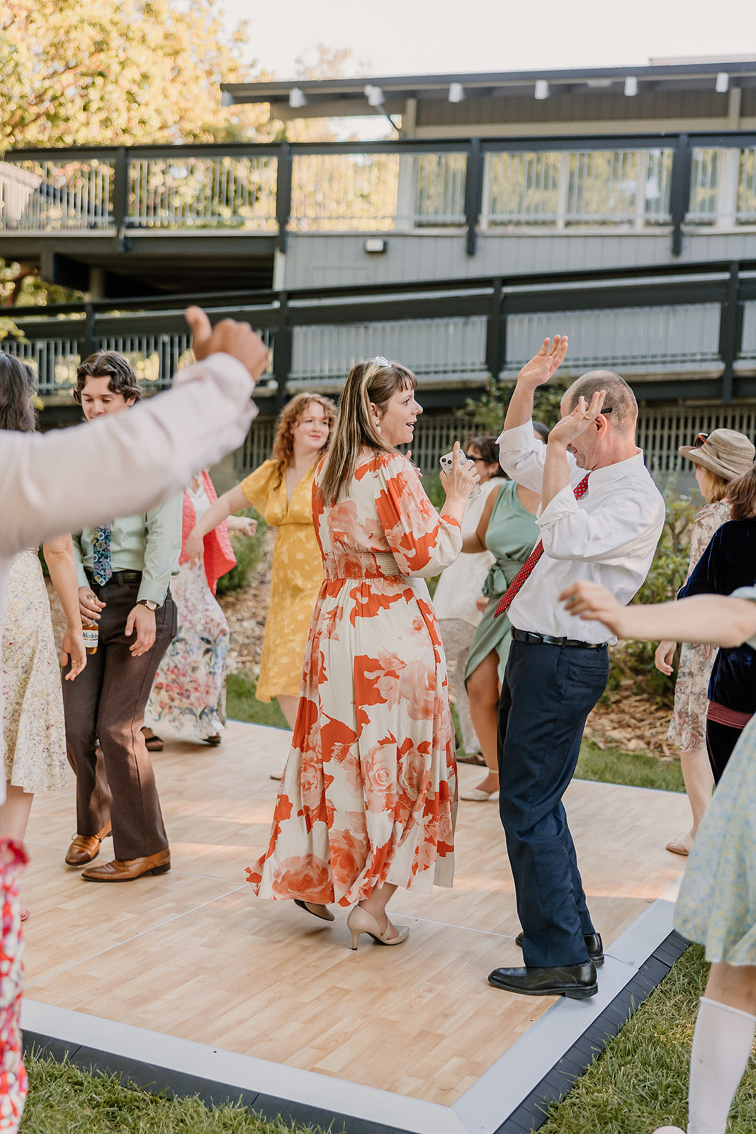 A group of people, including adults and children, are dancing outdoors on a wooden platform. at a wedding at the gardens at heather farms