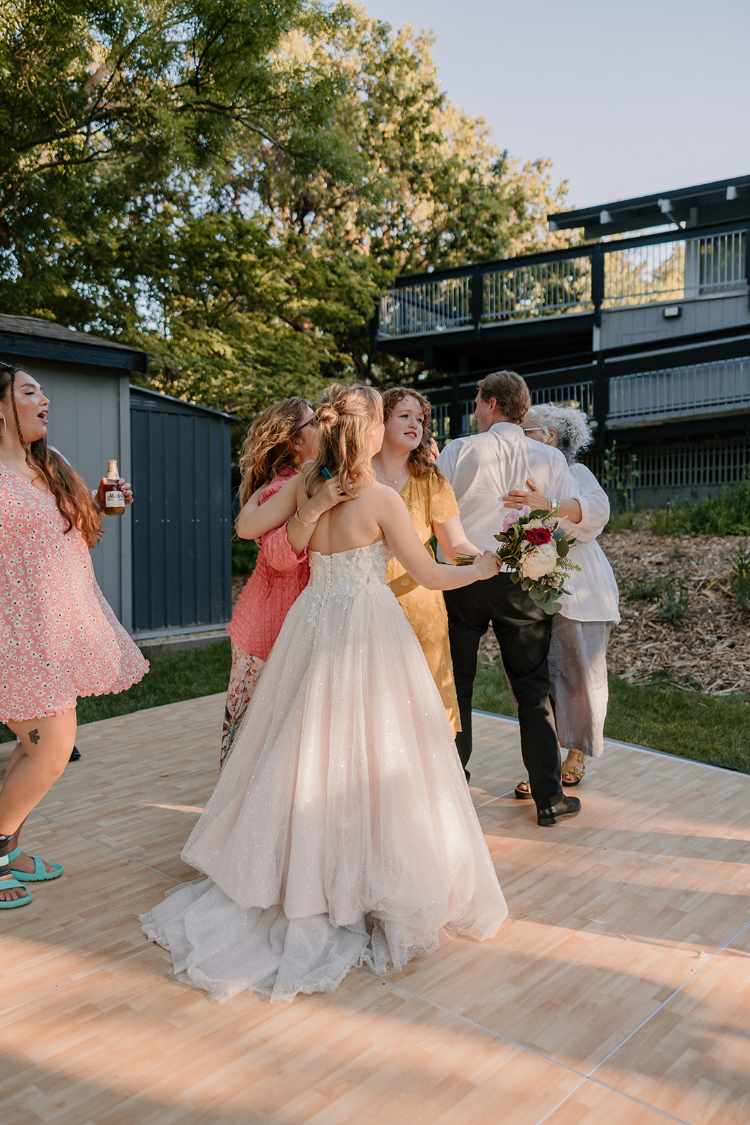 A group of people, including adults and children, are dancing outdoors on a wooden platform. at a wedding at the gardens at heather farms