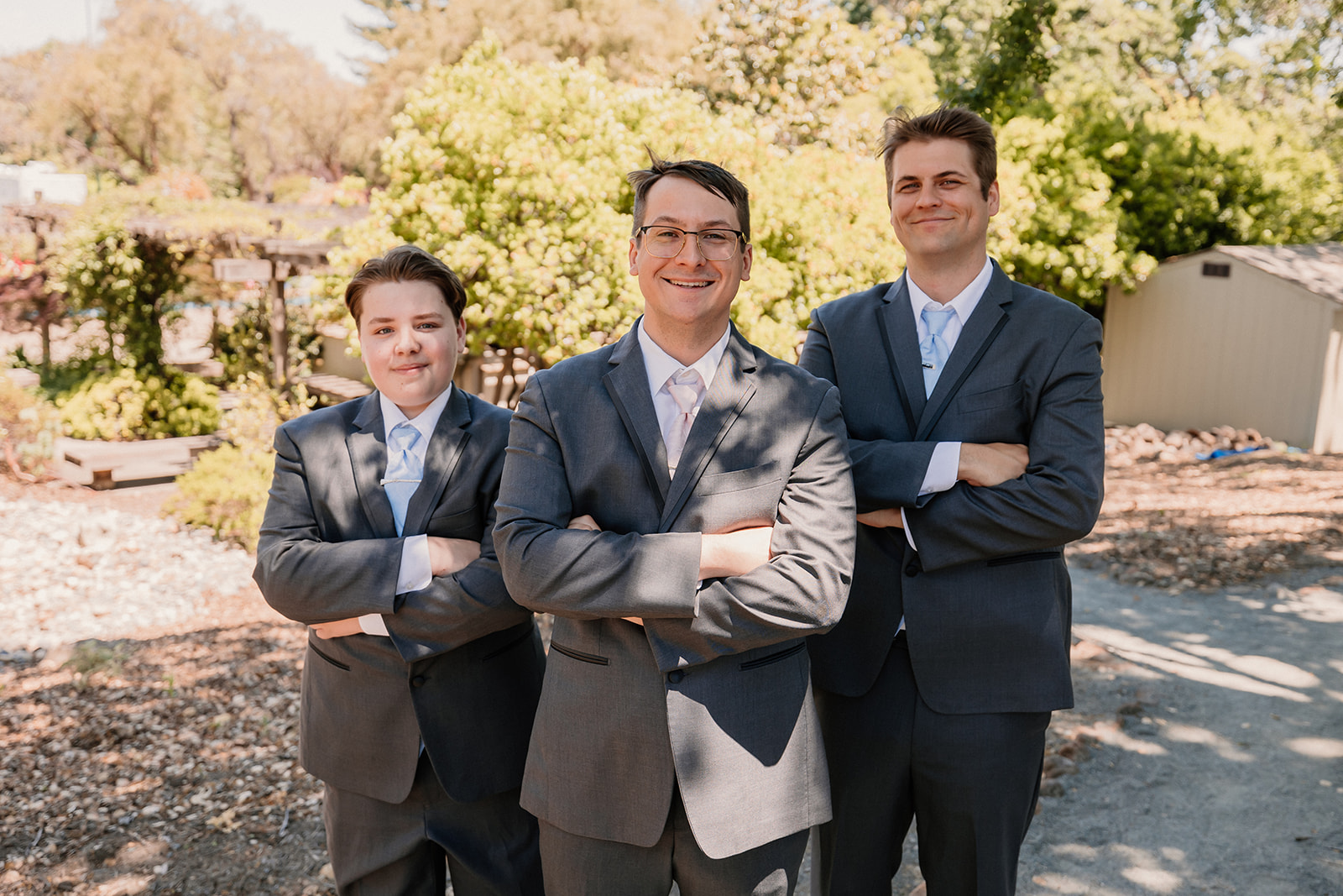 Three people in suits stand outdoors on a sunny day, 