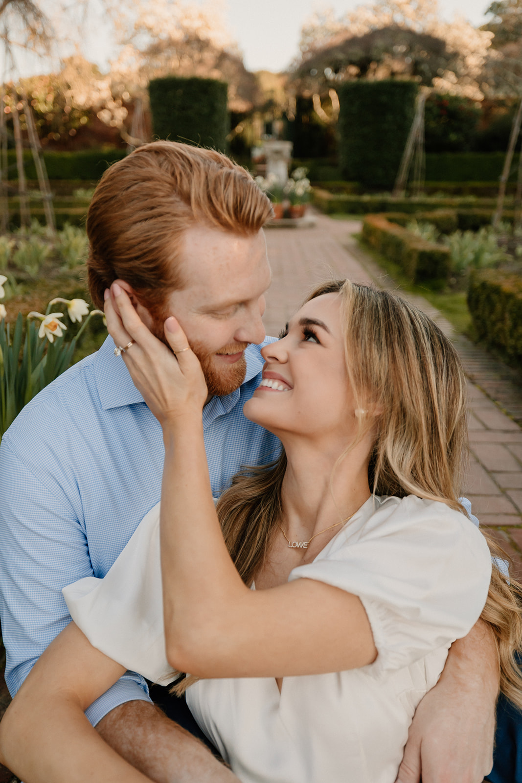 A couple embracing and smiling at, taking their engagement photos, both dressed in casual attire.