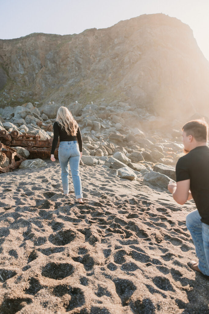 a couple posing for their proposal photos on the beach