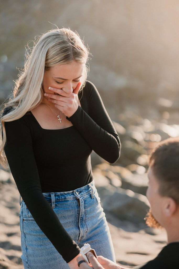 a couple posing for their proposal photos on the beach
