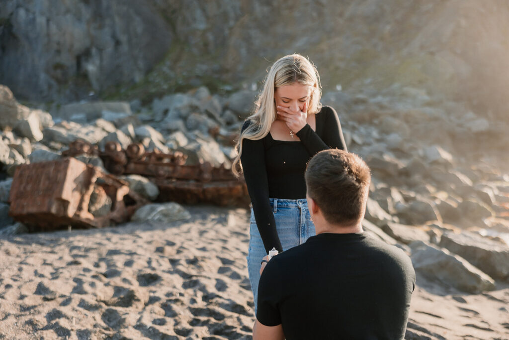 a couple posing for their proposal photos on the beach
